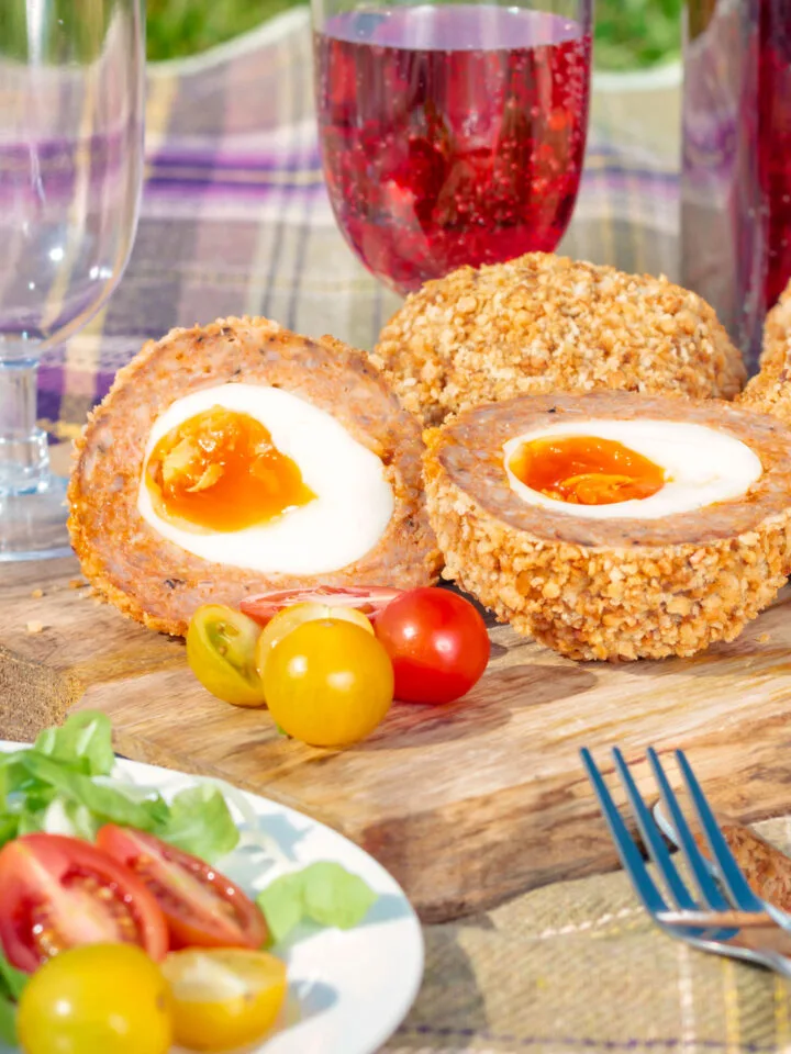 A scotch egg cut in half on a wooden board with a glass of red wine in the background.