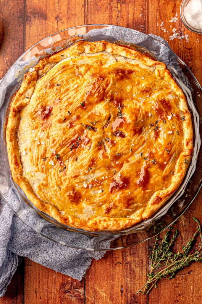 A steak and onion pie in a glass dish on a wooden background.