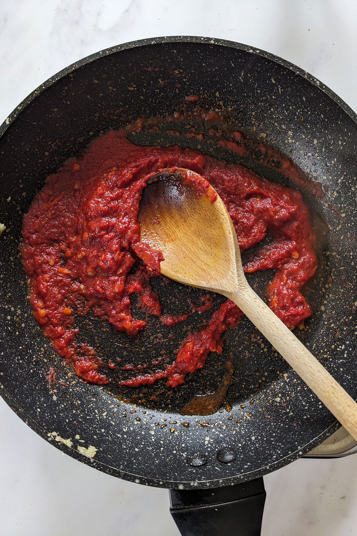 Stirring in the tomato paste and the vodka with a wooden spoon in a dark coloured frying pan.