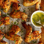 Garlic Butter Wings served topped with parsley and side dishes of parsley and melted butter and garlic sauce on a newspaper themed background.