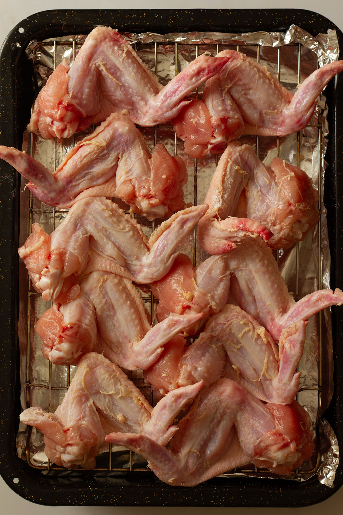 Wings prepared prior to cooking, on a wire rack on a tray lined with kitchen foil.