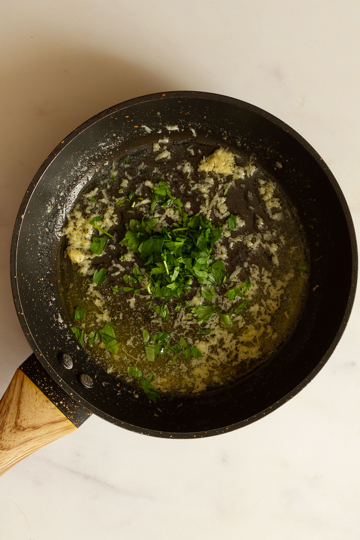 Preparing the melted butter and garlic sauce with added parsley in a dark coloured saucepan.