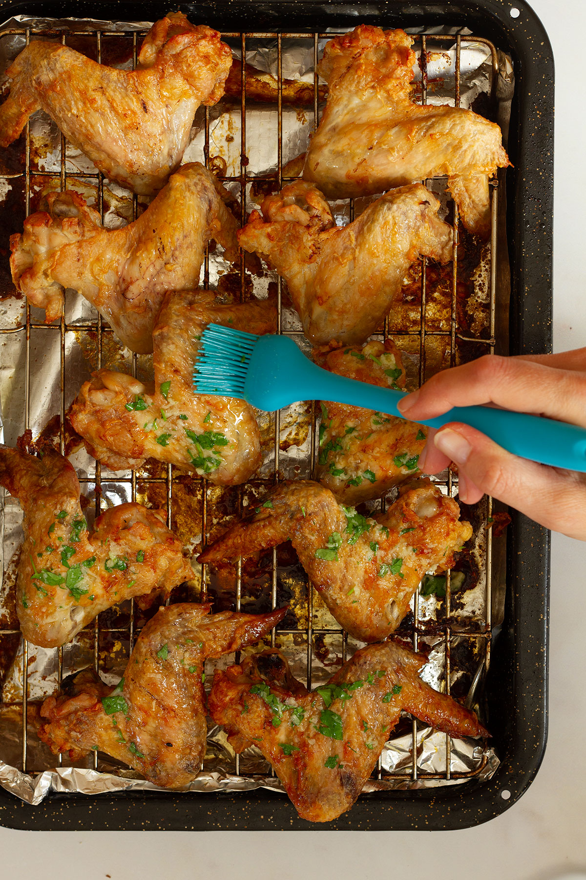Brushing the cooked chicken wings with the garlic butter sauce using a blue silicone brush.