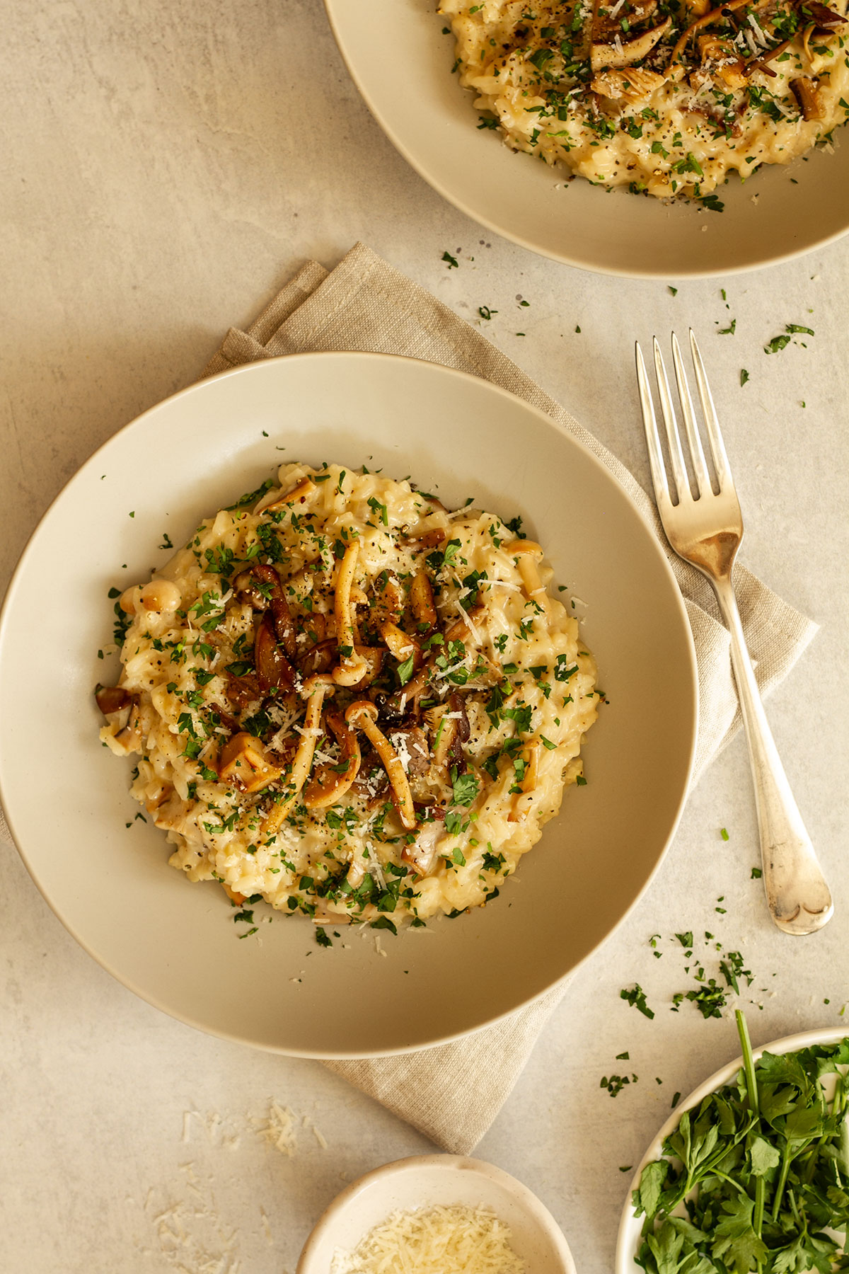 Two servings of Mushroom Risotto on cream coloured plates with parsley and Parmesan.