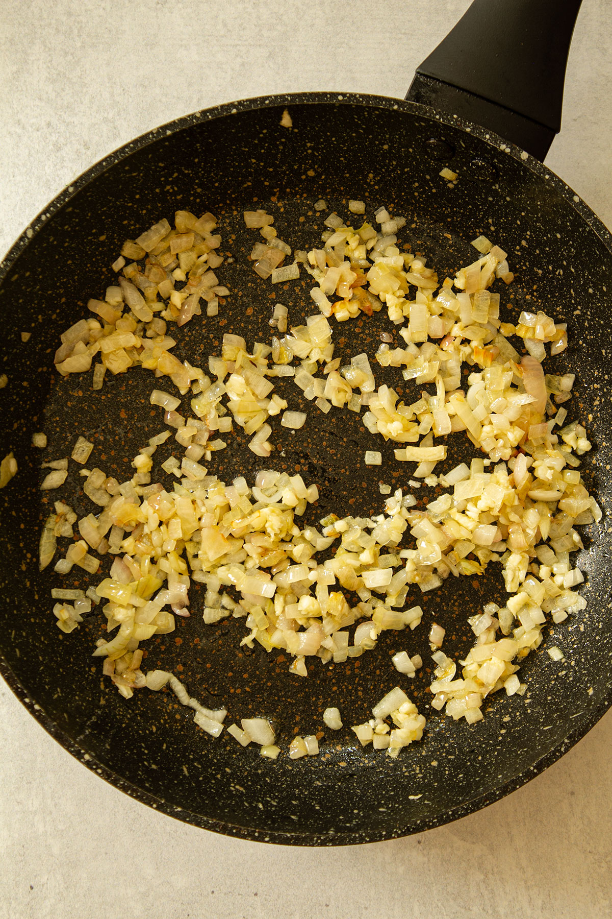 Sautéing the onions in a dark coloured frying pan.