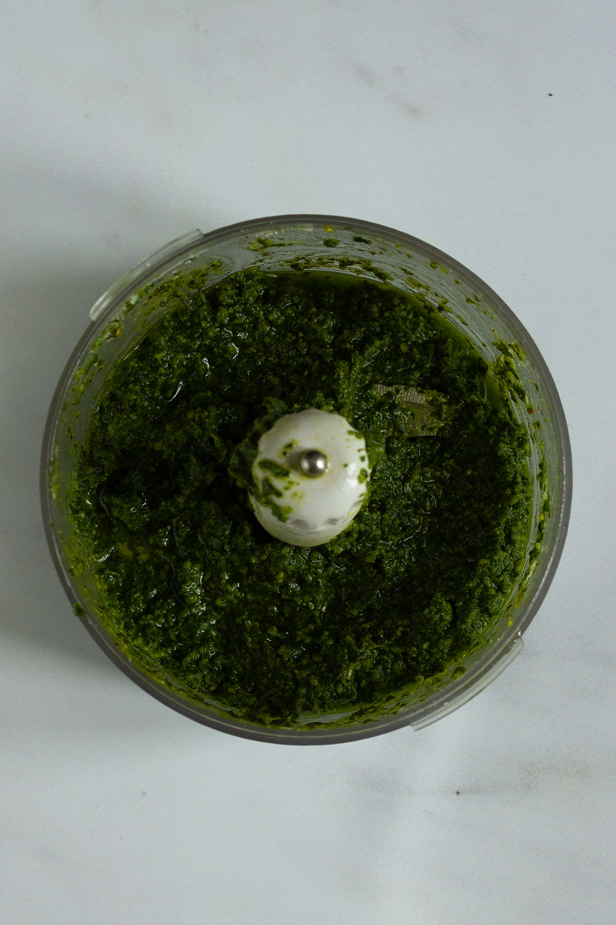 Blending the pesto with olive oil in a food processor until it reaches the desired consistency.