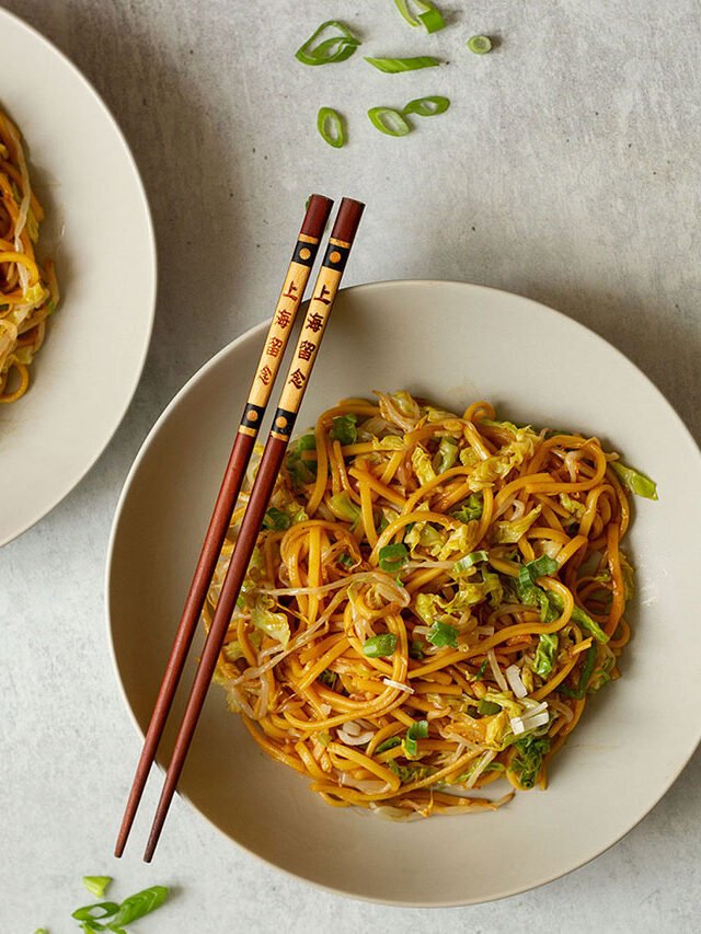 Plain Chow Mein Noodles topped with extra scallions, served on a white plate with brown chopsticks.