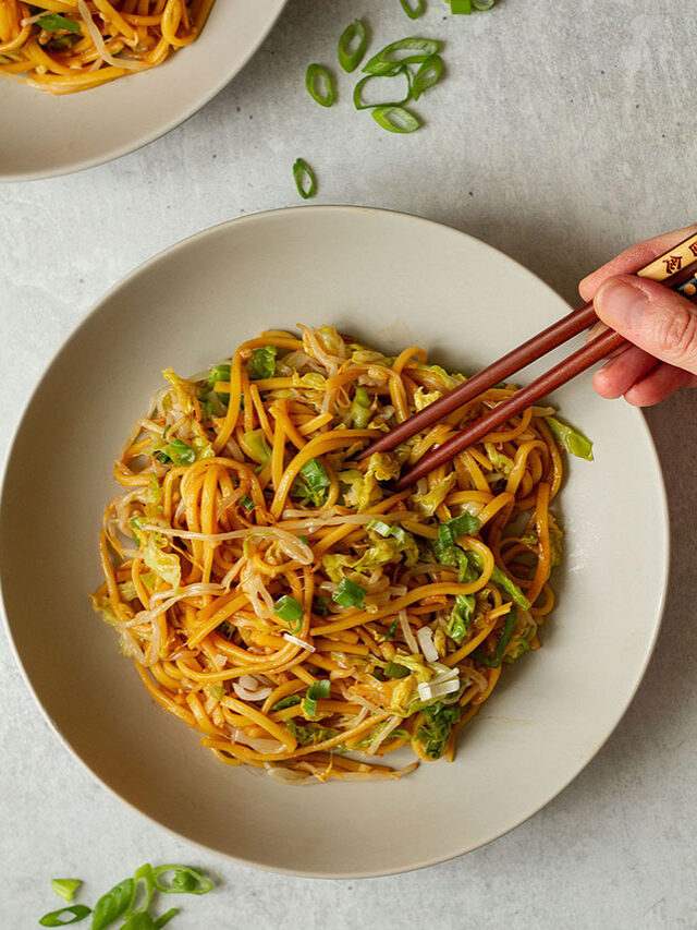 Plain Chow Mein Noodles topped with extra scallions, served on a white plate with brown chopsticks.