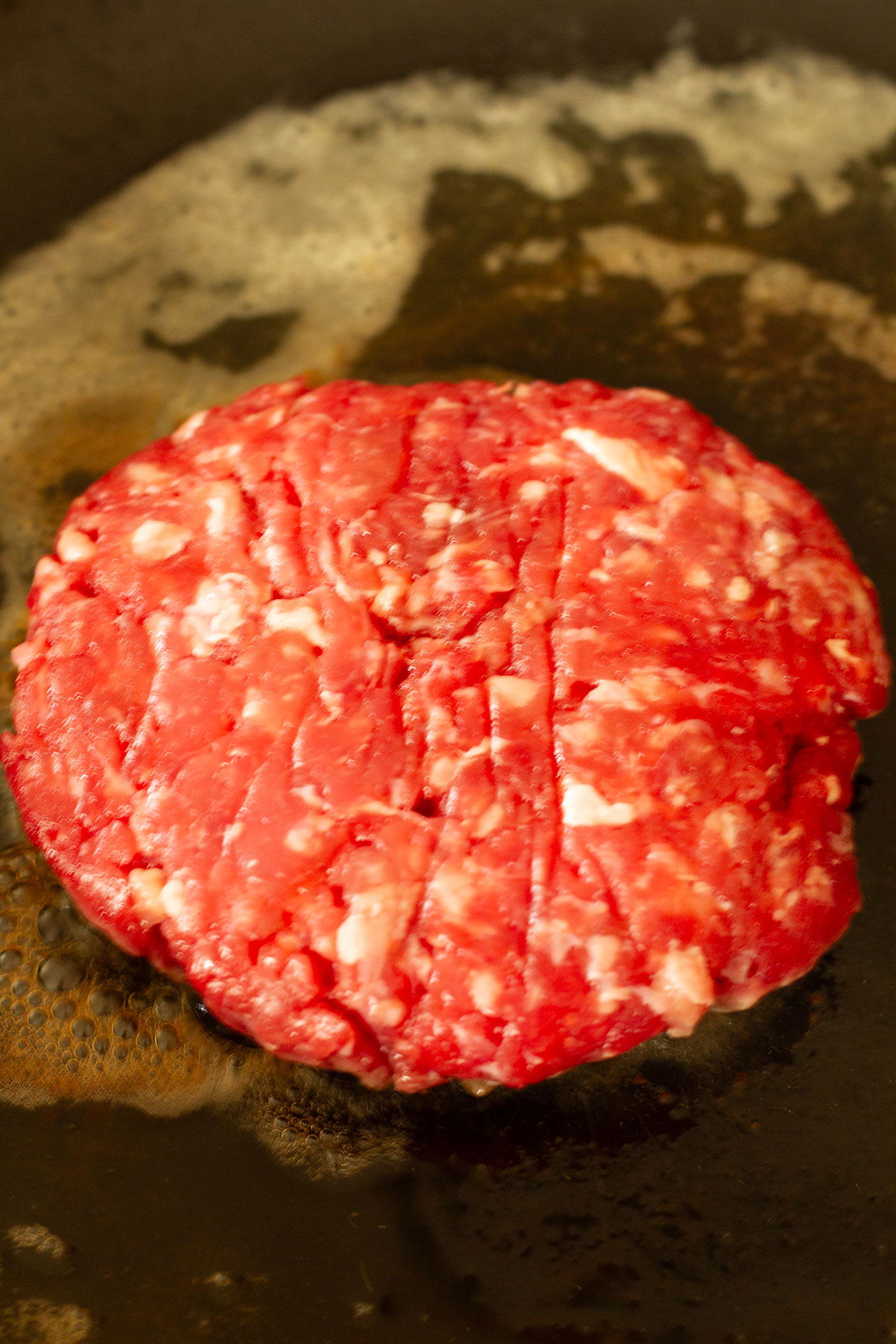 A burger pattie being friend in butter in a cast iron skillet.