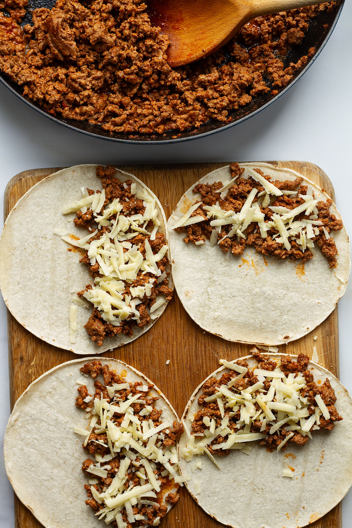 Placing spoonfuls of the beef filling onto each tortilla, and adding a little shredded cheese.