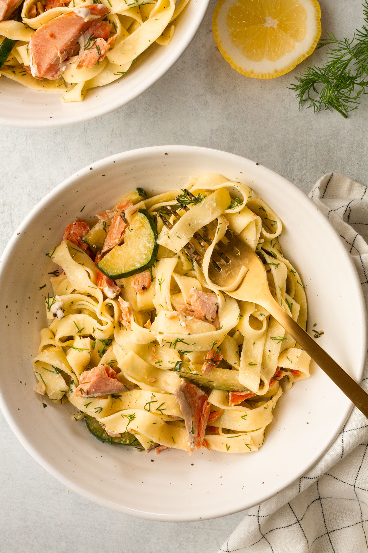 A serving of salmon and dill pasta in a white bowl with a slice of lemon on the side.