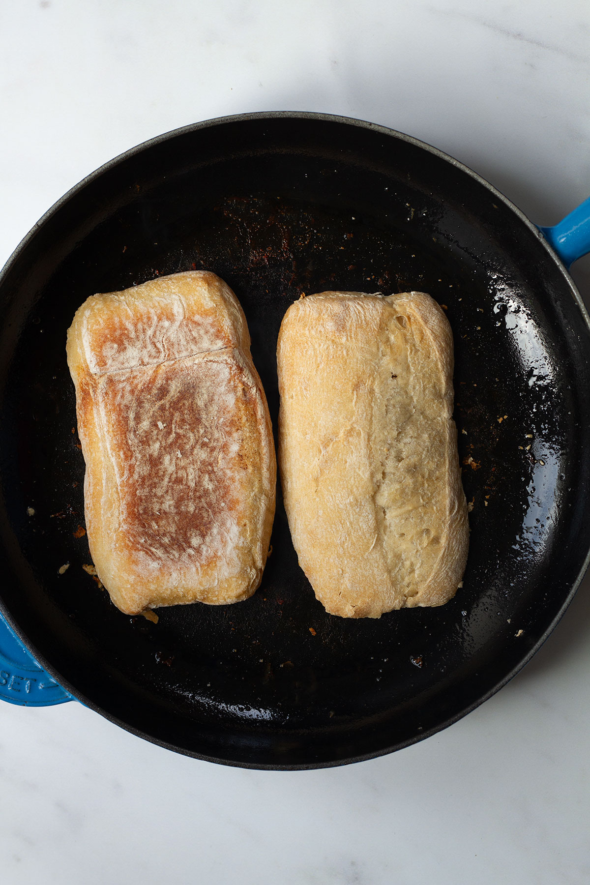 Toasting the sliced ciabatta rolls face-down in a dark coloured frying pan.