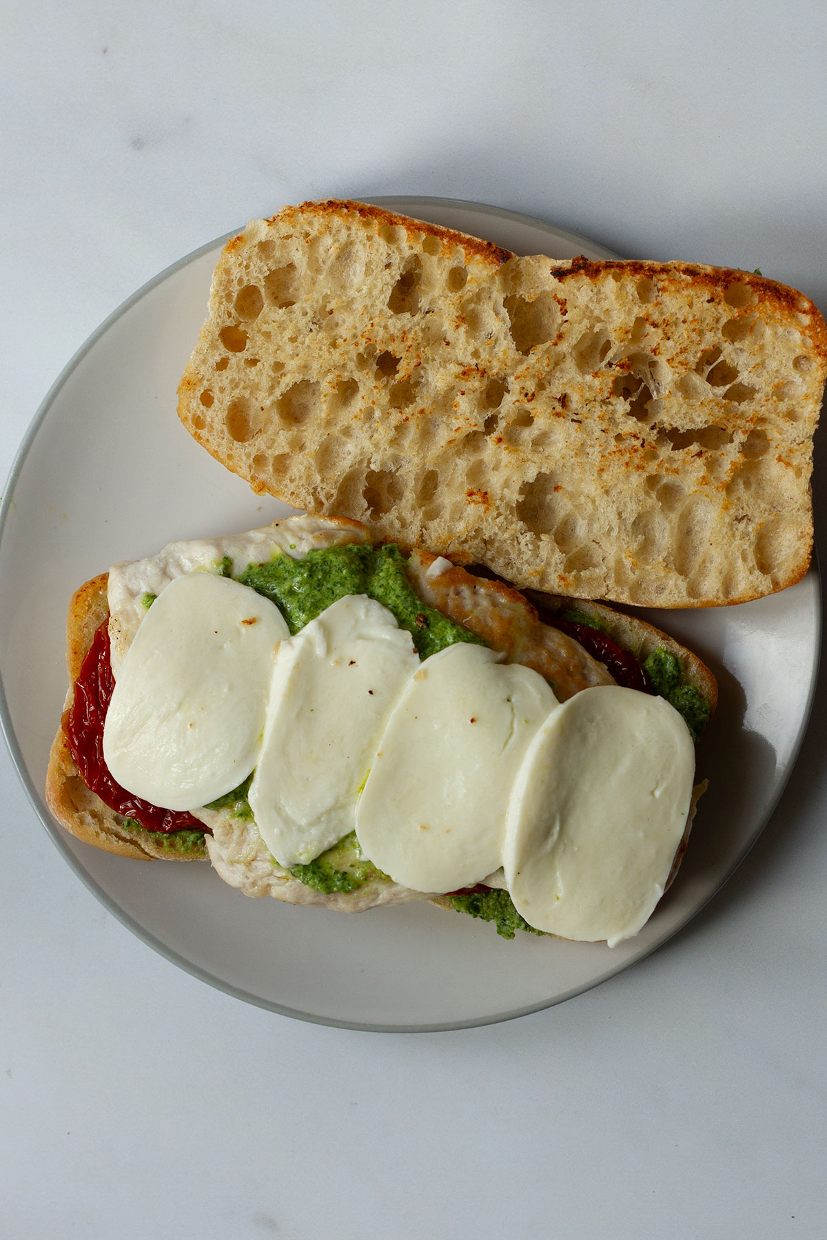 The assembled sandwich ready to serve showing the pesto sauce, sun-dried tomatoes, chicken, and mozzarella.