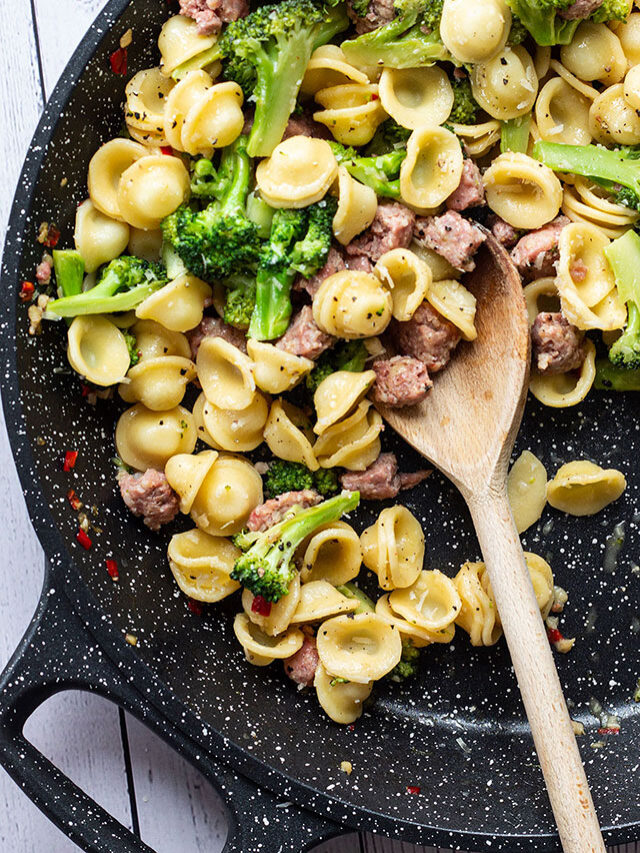 A pan of broccoli and sausage pasta with a wooden spoon.