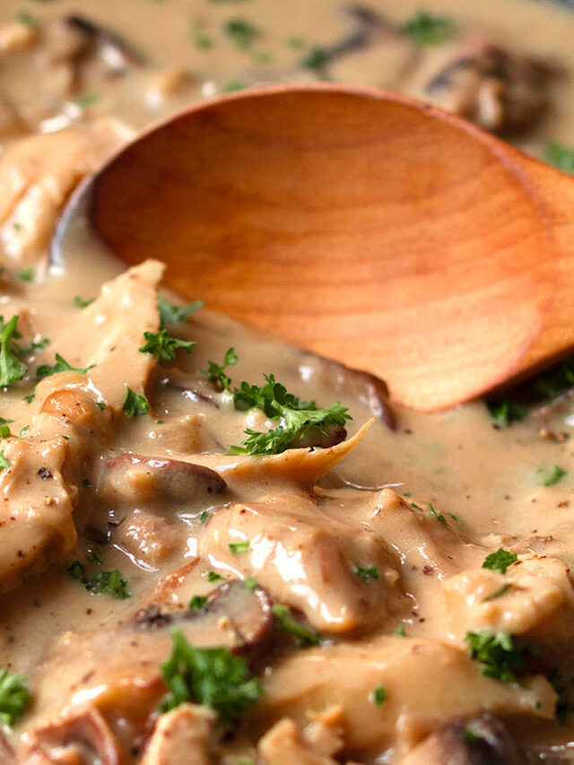 A close up photograph of turkey fricassee garnished with parsley, being served with a wooden spoon.