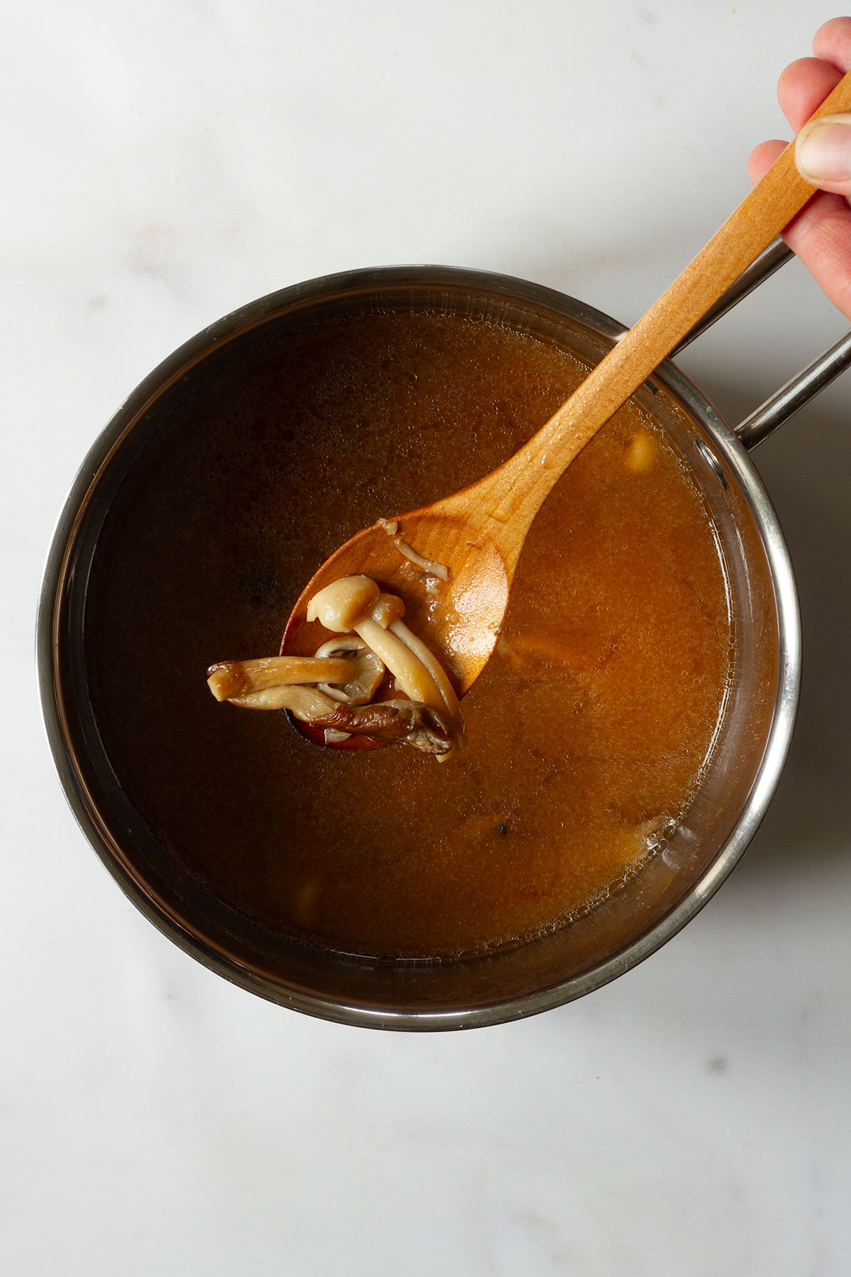 A pan of miso soup with mushrooms added on a white background.