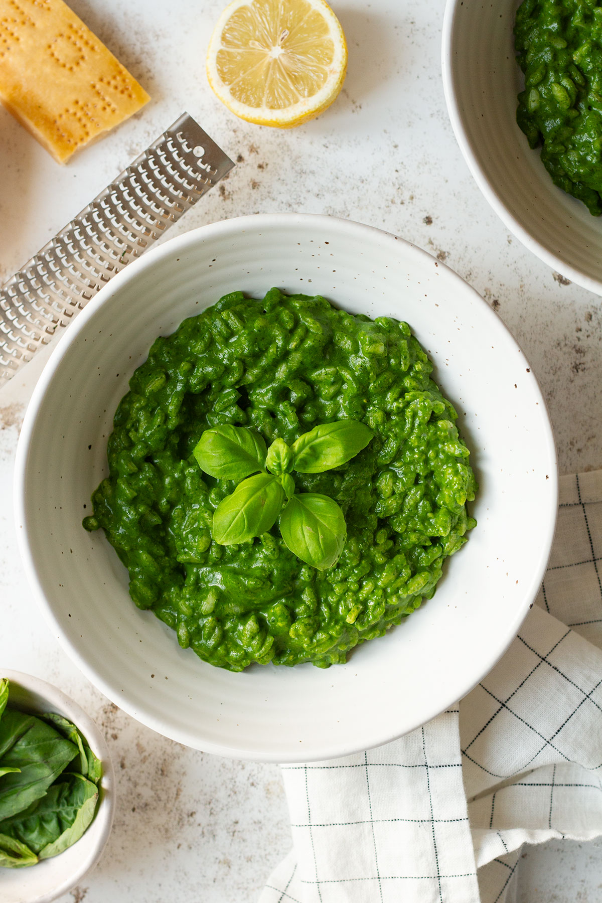 Risotto Verde with a basil garnish served in a white bowl with lemon and Parmesan on the side.