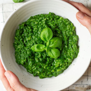 A bowl of green spinach risotto on a white background.