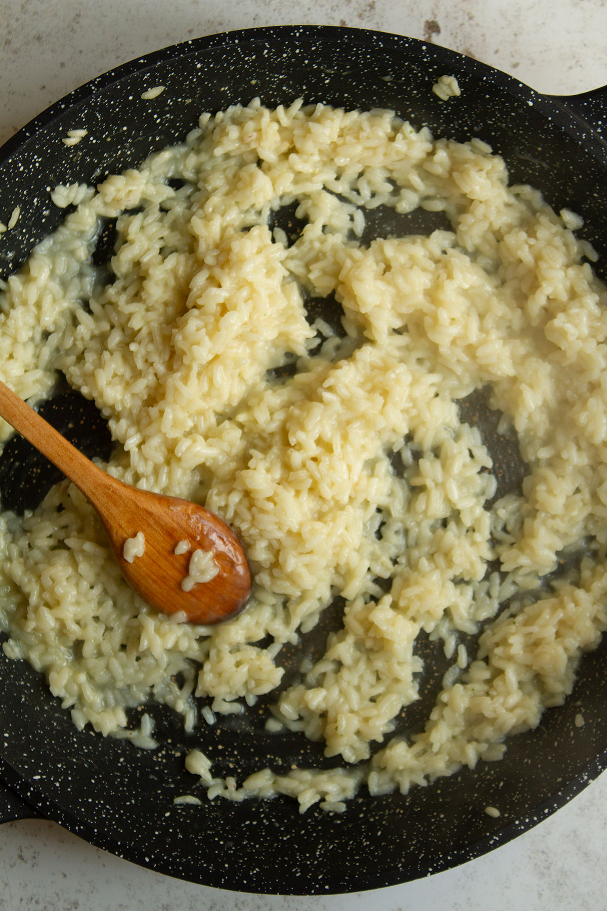 Stirring the rice with the added hot vegetable stock with a wooden spoon in a dark coloured skillet.