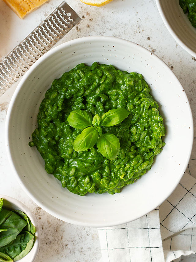 Risotto Verde with a basil garnish served in a white bowl with lemon and Parmesan on the side.