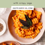 Two bowls of Roast Pumpkin Pasta topped with crispy sage leaves on a white and chequered cloth. background.