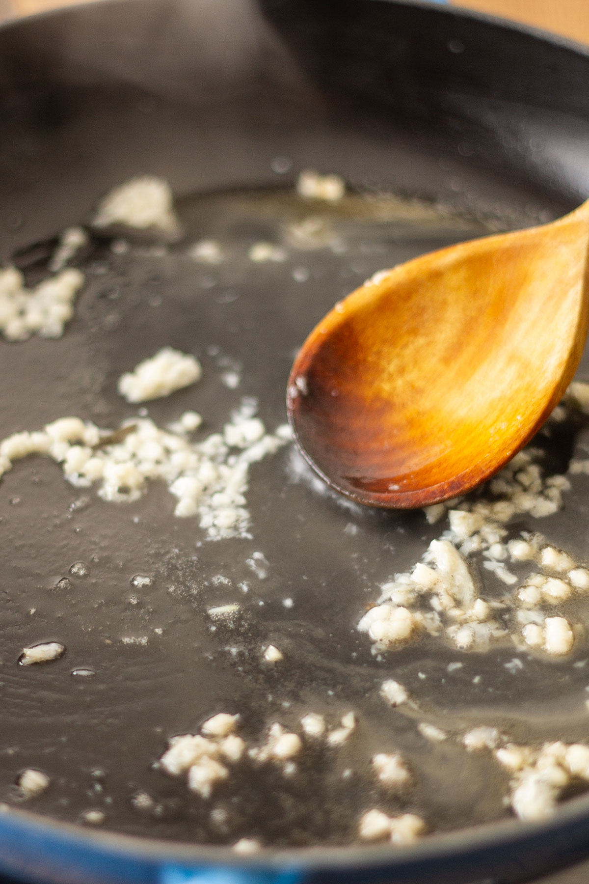 Sauteeing the minced garlic and stirring with a wooden spoon in a skillet.