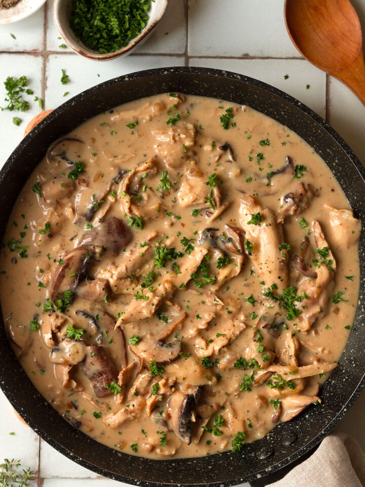 Turkey fricassee garnished with parsley, in a dark coloured pan on white tiled background, ready to serve.