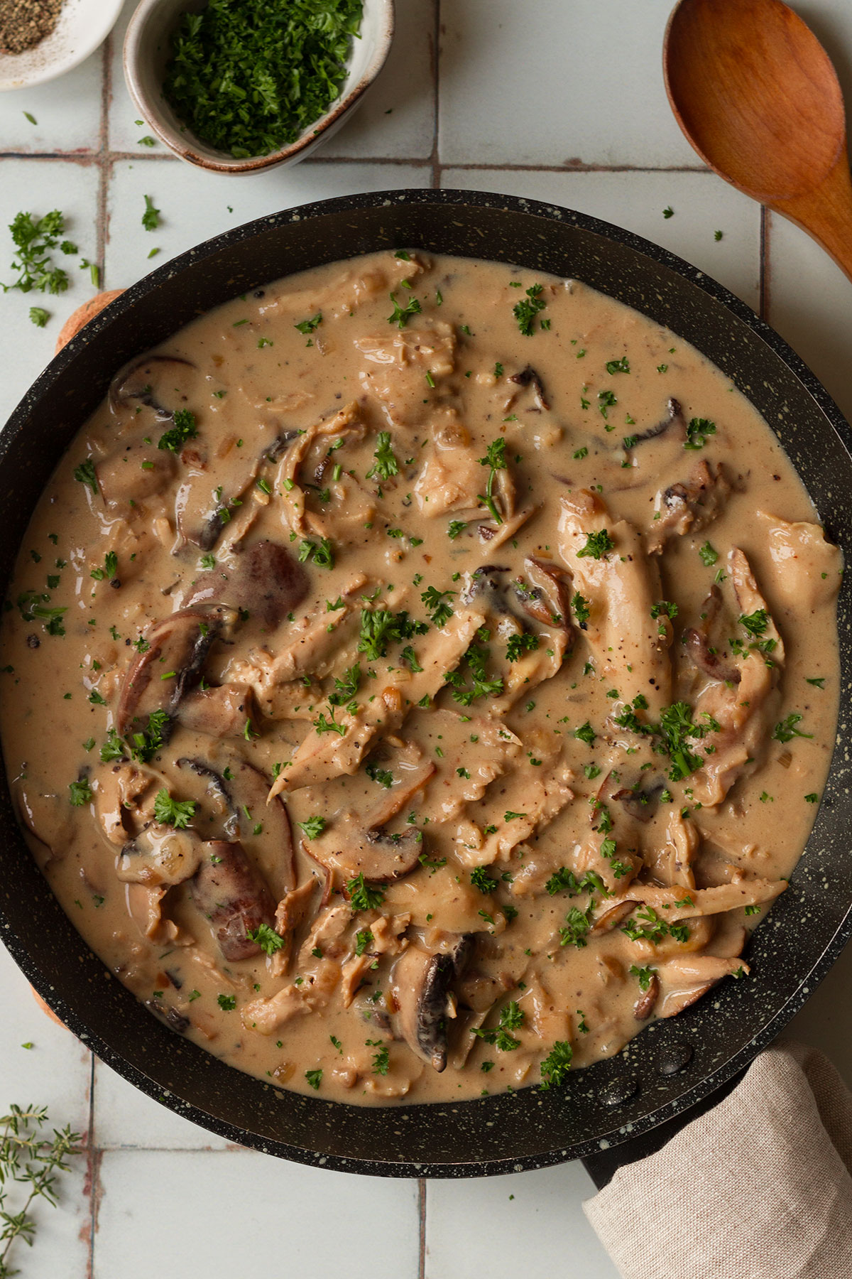 Turkey fricassee garnished with parsley, in a dark coloured pan on white tiled background, ready to serve.