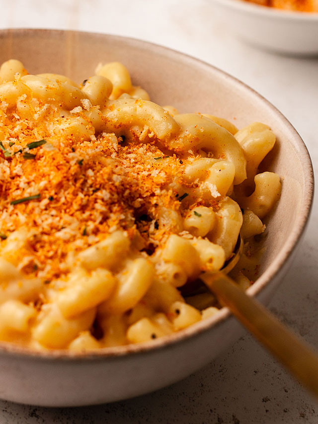 Close up photograph of Mac and cheese served in a bowl on a white background.