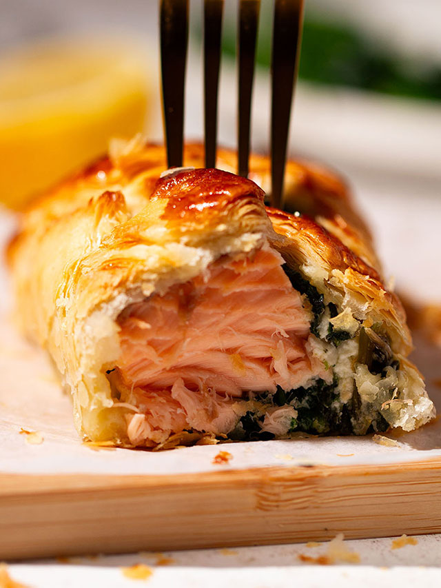 A serving of a portion of Salmon Wellington on a wooden board.