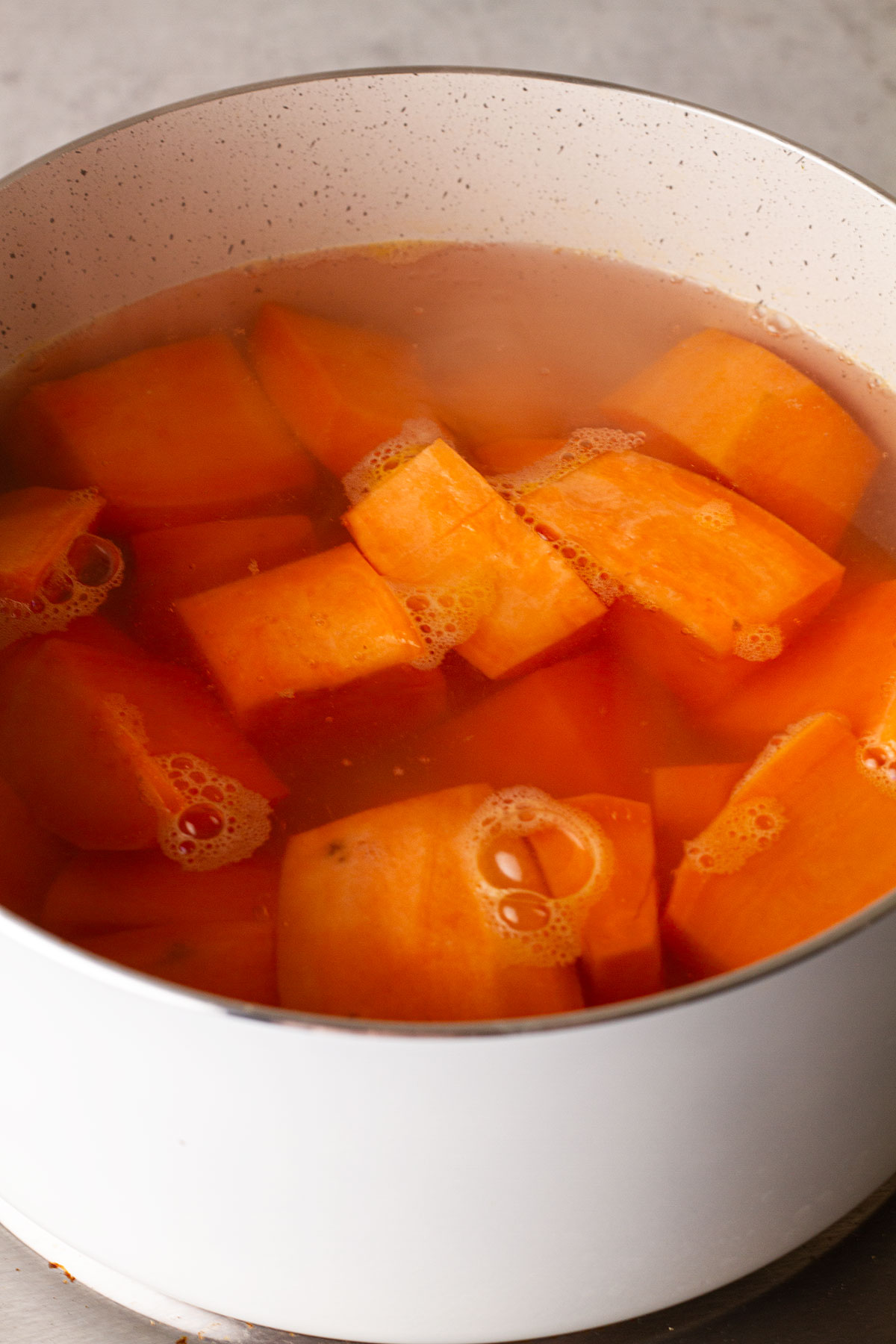 Boiling the sweet potatoes until fork tender in a white cooking pot.