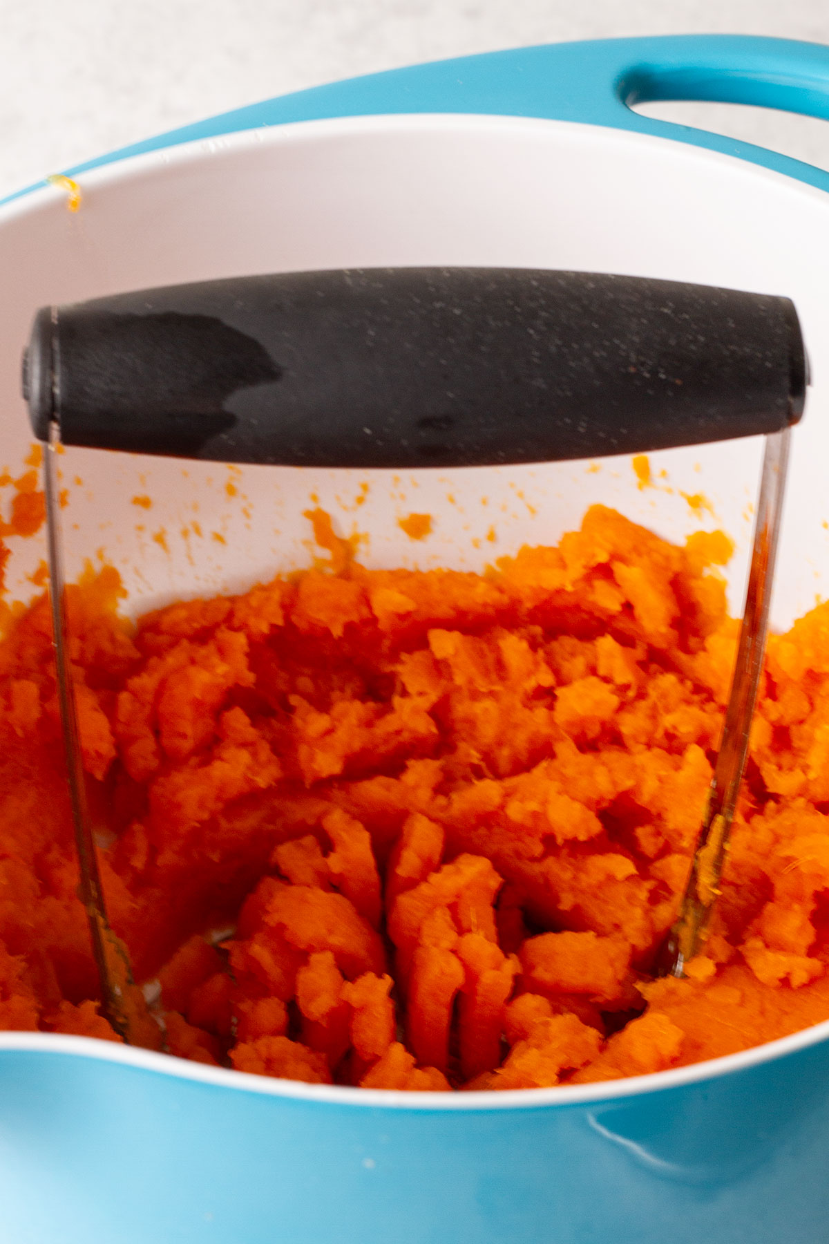 Mashing the cooked sweet potatoes in a blue and white bowl.
