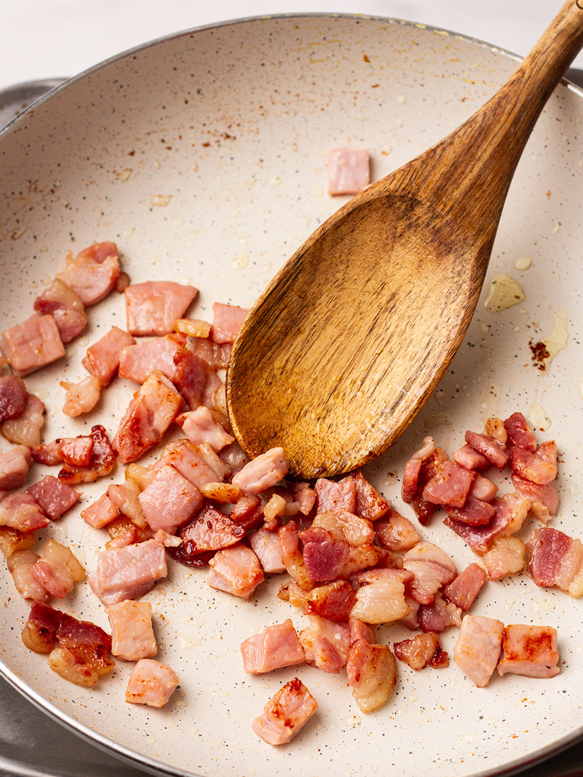 Stirring the frying bacon with a wooden spoon,over a medium heat until crispy.
