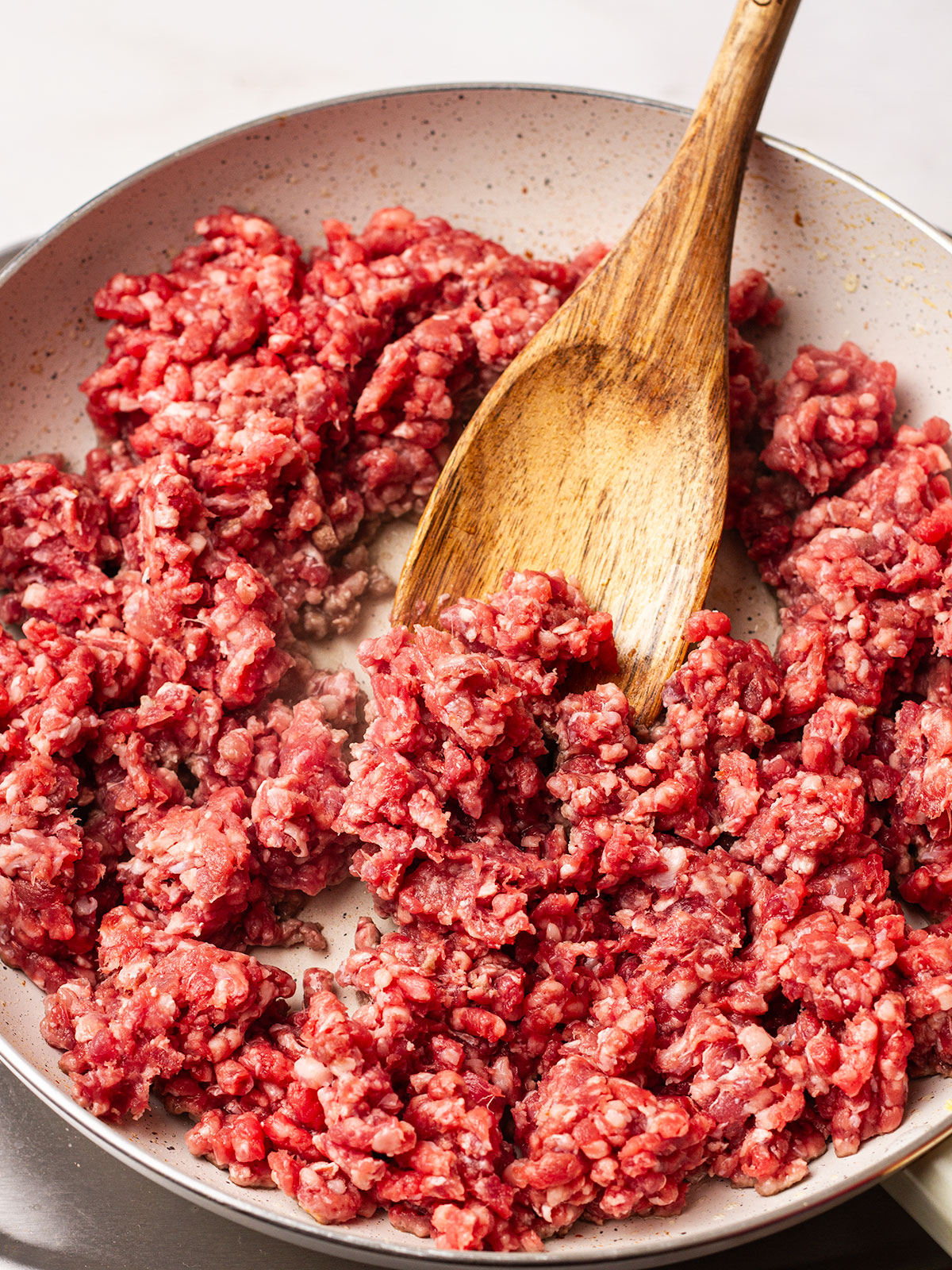 Stirring the browning ground beef with a wooden spoon over a high heat.