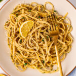 Lemon butter garlic pasta served with a wedge of lemon on a cream coloured plate.