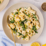 Lemon Ricotta Pasta with arugula served in a cream coloured bowl with lemon and pepper on the side.