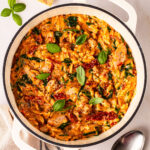Baked chicken orzo ready to serve with basil leaves on top. In a cream pot on a white background.