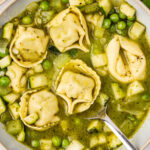 Close up of a serving of a serving of pesto tortellini soup. Served in In a white bowl.