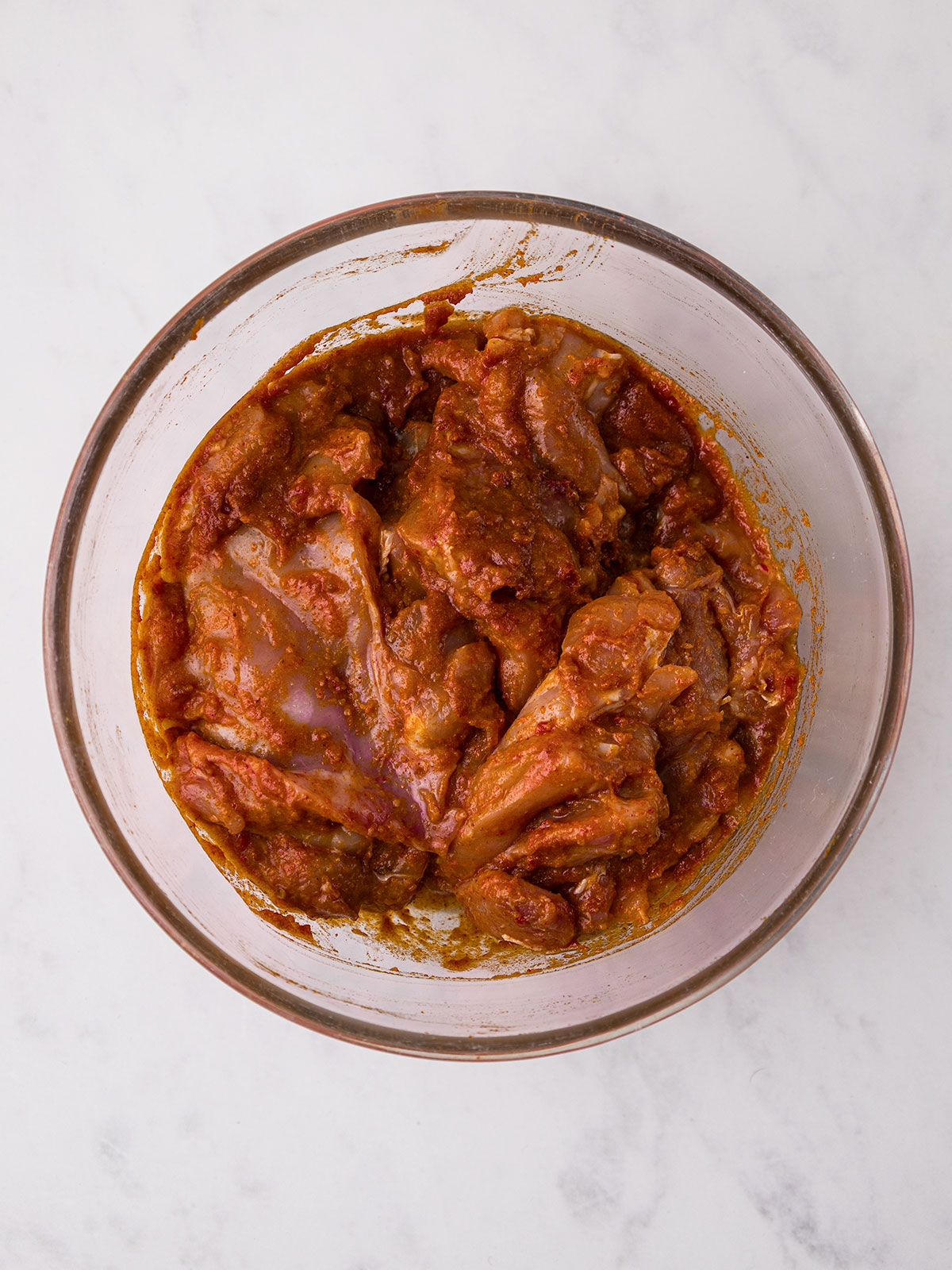 Marinating the chicken thighs for 30 minutes in a glass bowl on a white background.