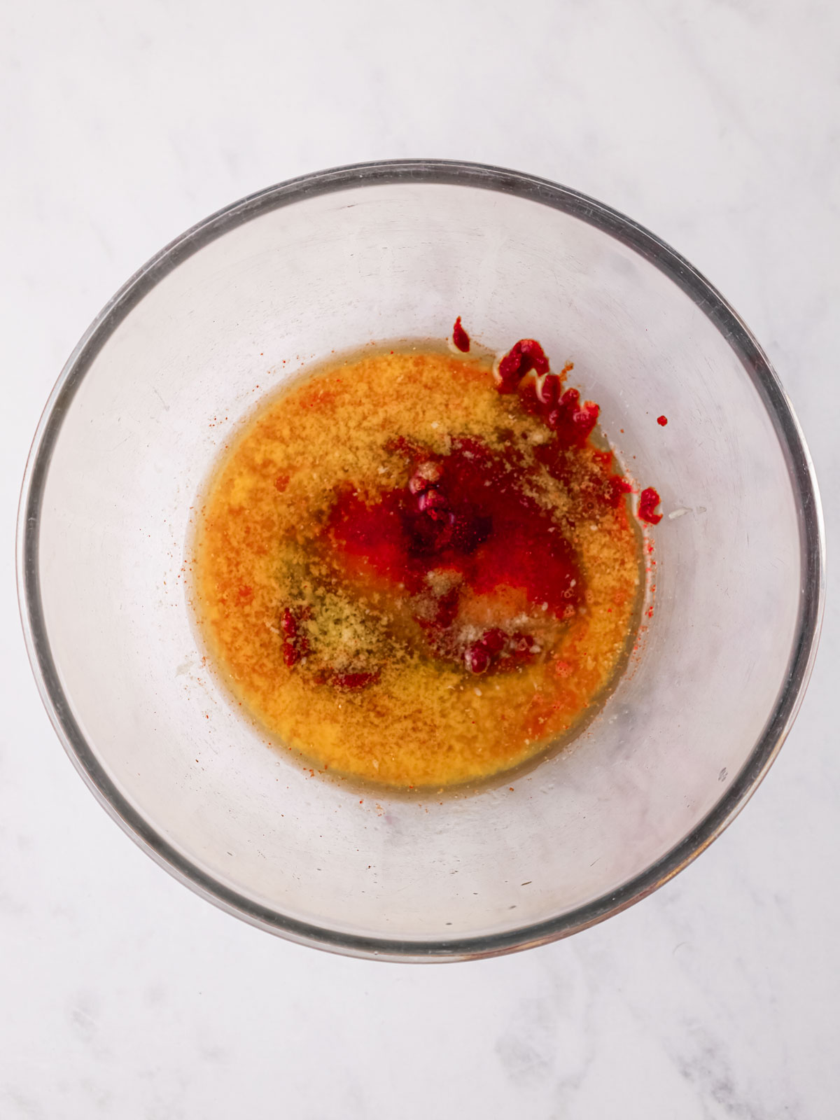 The marinade mixture of harissa paste, paprika, chili powder, garlic powder, salt, lime juice, melted butter, and honey in a glass bowl on a white background.