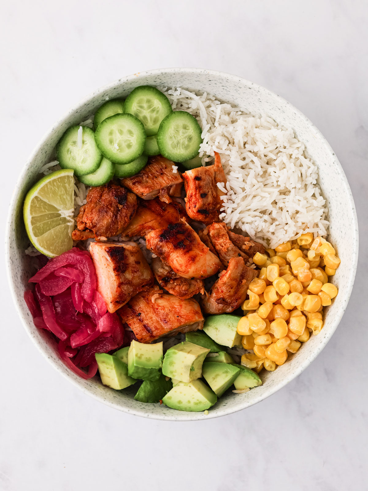 Harissa Honey Chicken cut into bite-sized pieces and served in a white Cava Bowl on a white background.