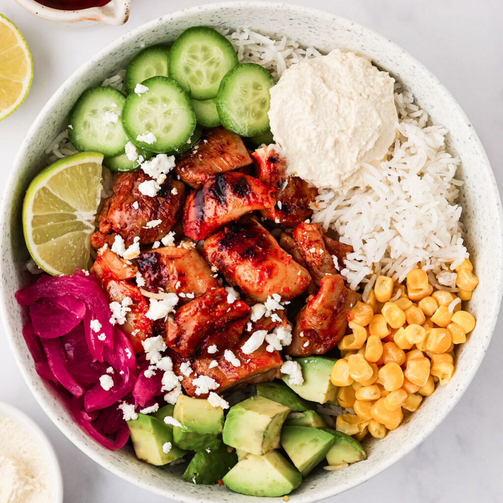 Harissa Honey Chicken cut into bite-sized pieces and served in a white Cava Bowl on a white background.