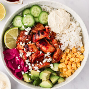 Harissa Honey Chicken cut into bite-sized pieces and served in a white Cava Bowl on a white background.
