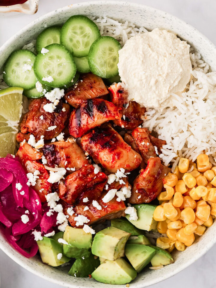 Harissa Honey Chicken cut into bite-sized pieces and served in a white Cava Bowl on a white background.