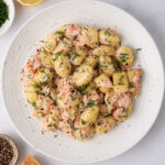A serving of Creamy Salmon Gnocchi on a white plate with lemon, pepper, Parmesan and dill on the side.