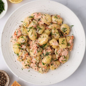 A serving of Creamy Salmon Gnocchi on a white plate with lemon, pepper, Parmesan and dill on the side.