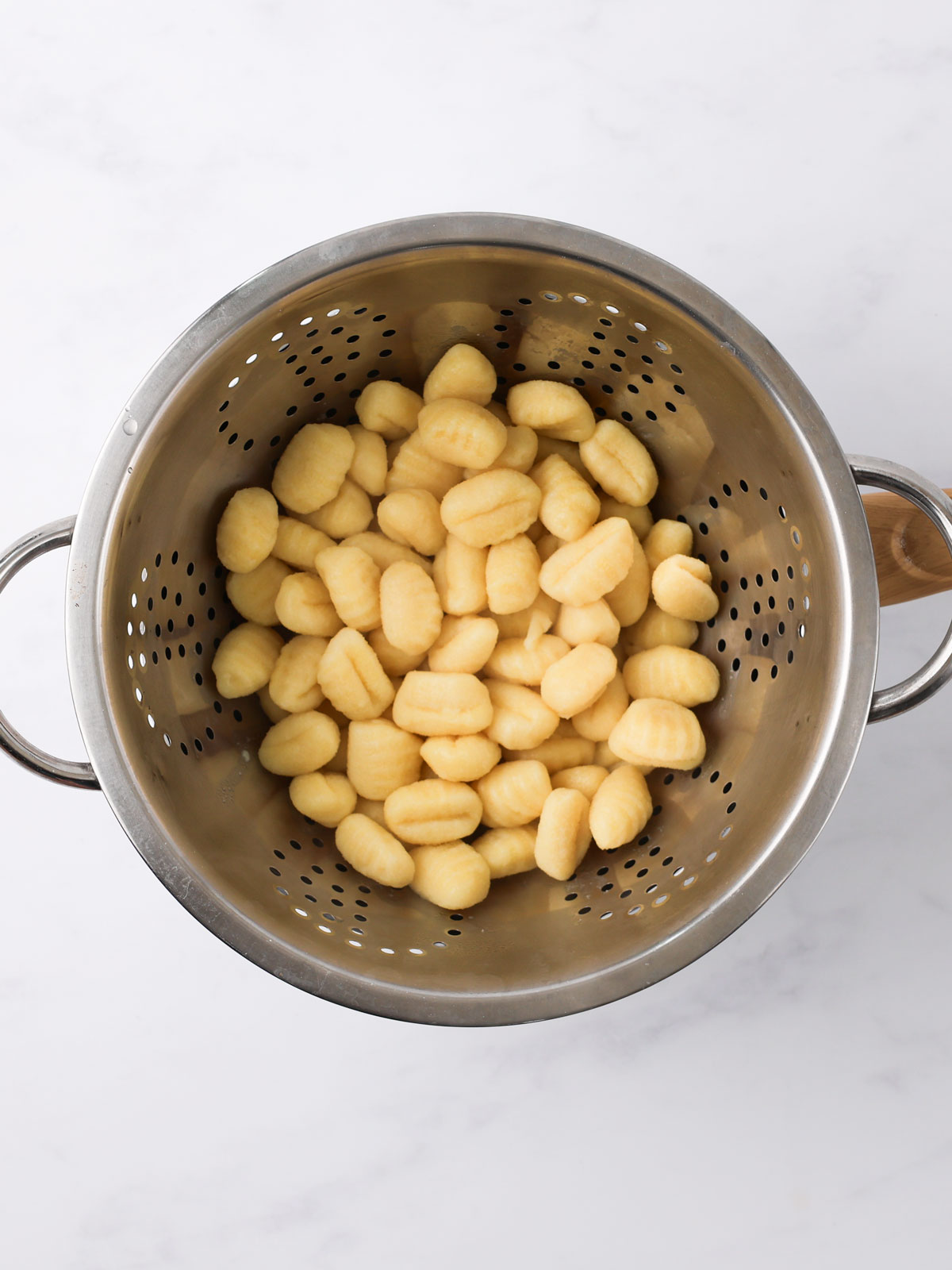 Draining the cooked gnocchi in a silver coloured colander.