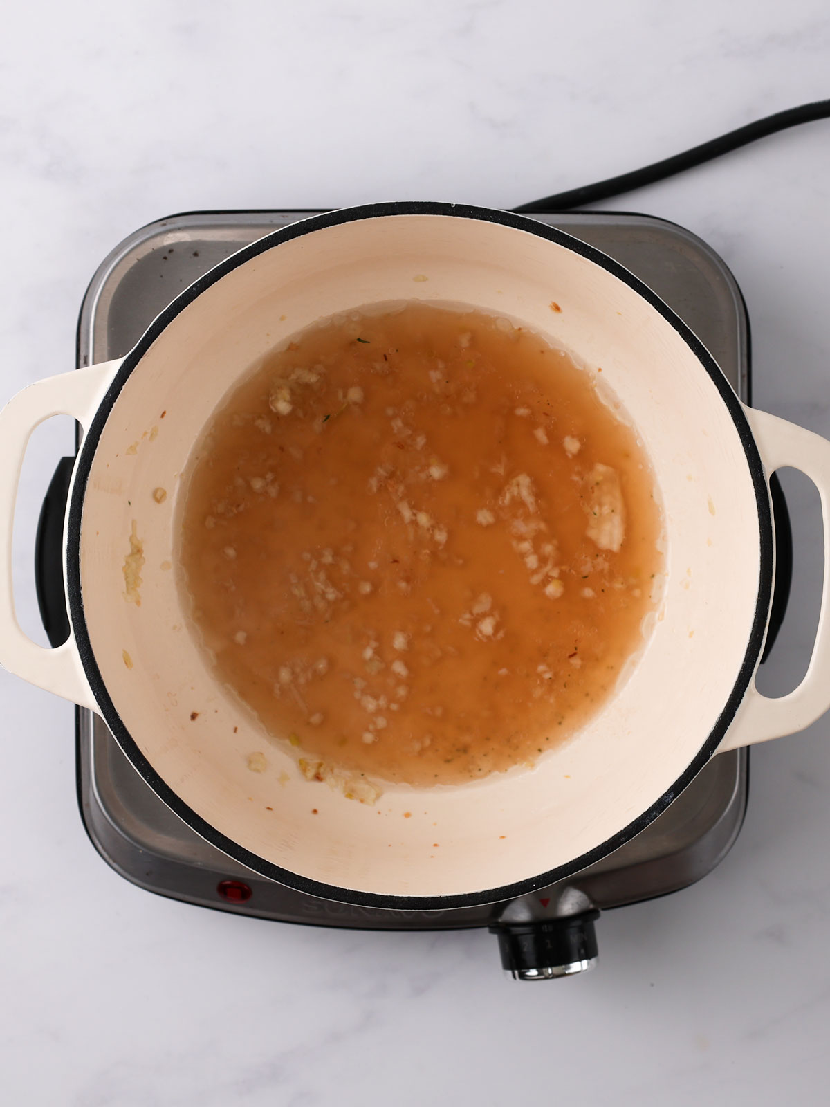 The fried garlic and chicken stock in a white enamel bowl on an electric hot plate.