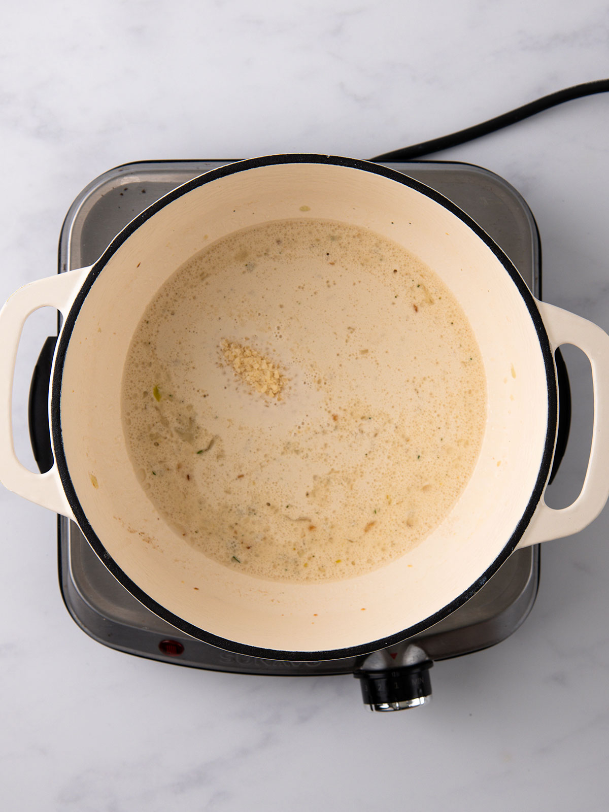 Adding the cream, Parmesan and dill in a white enamel bowl on an electric hot plate .