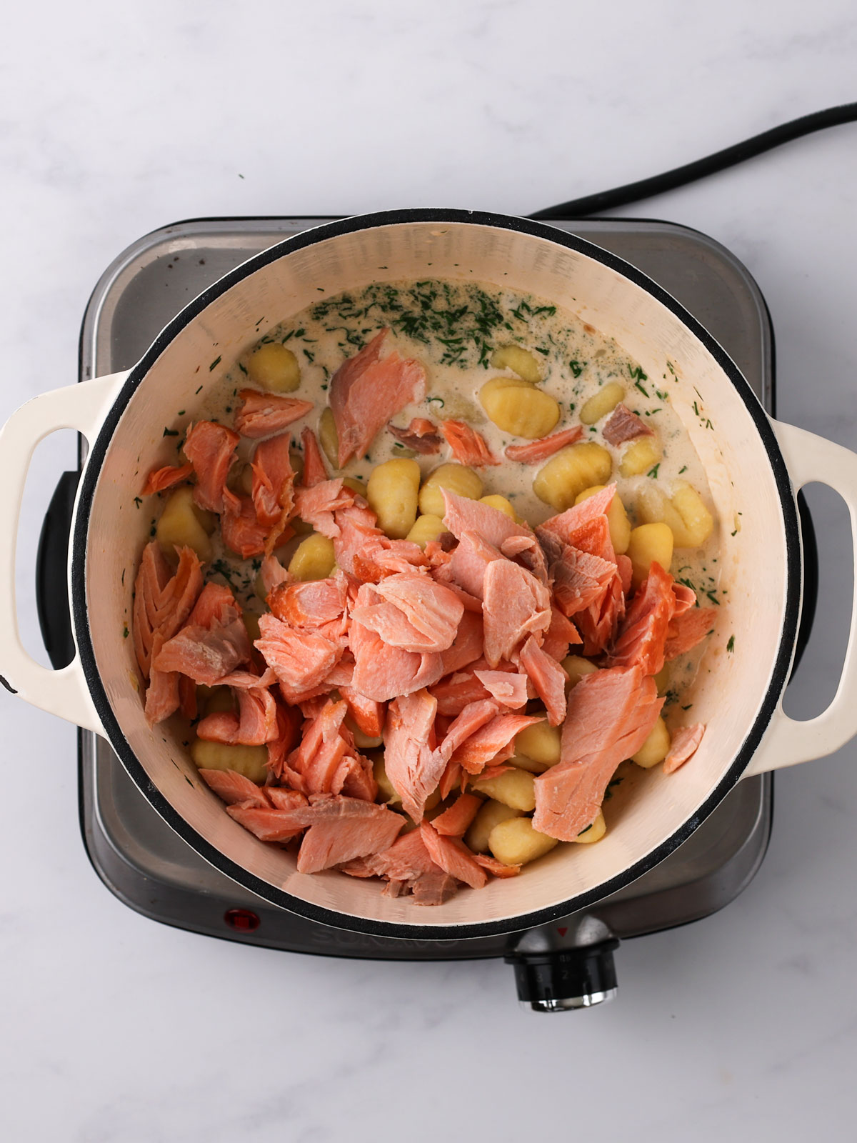 Stirring in the gnocchi and salmon in a white enamel bowl on an electric hot plate.